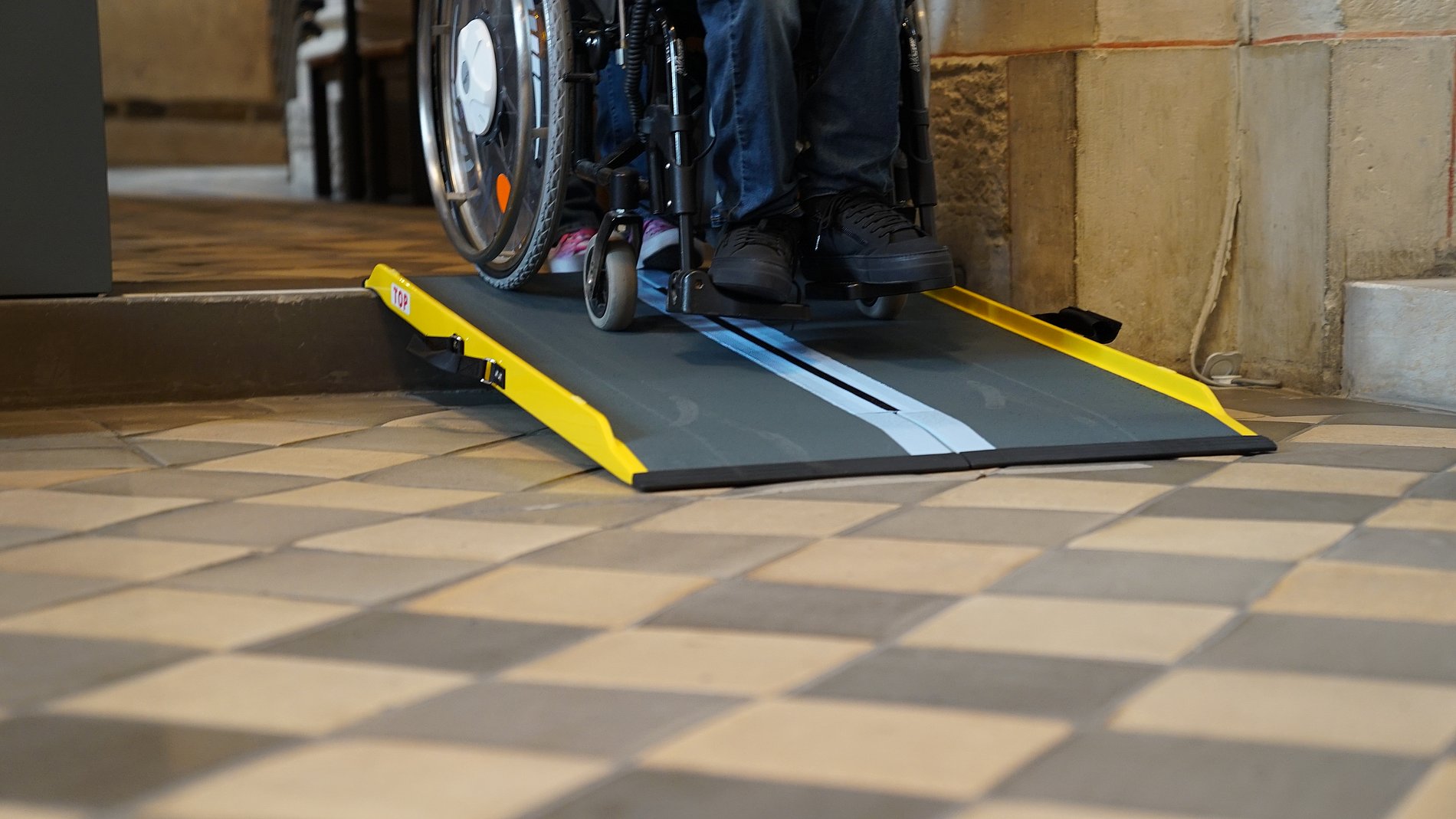 eine Rampe an einer Stufe wo man Rollstuhlräder runter fahren sieht