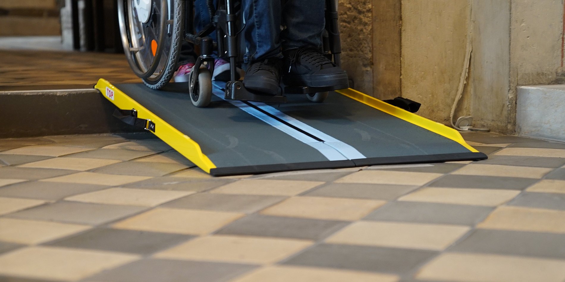 eine Rampe an einer Stufe wo man Rollstuhlräder runter fahren sieht
