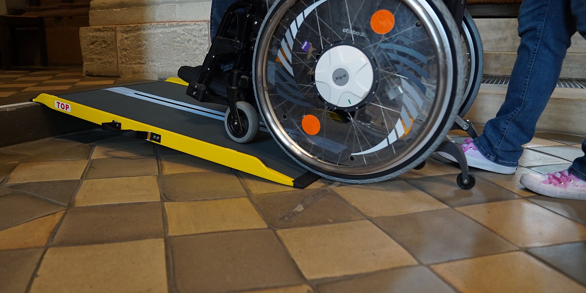 Rampe an einer Stufe mit Rollstuhlrädern am Fußende von der Seite
