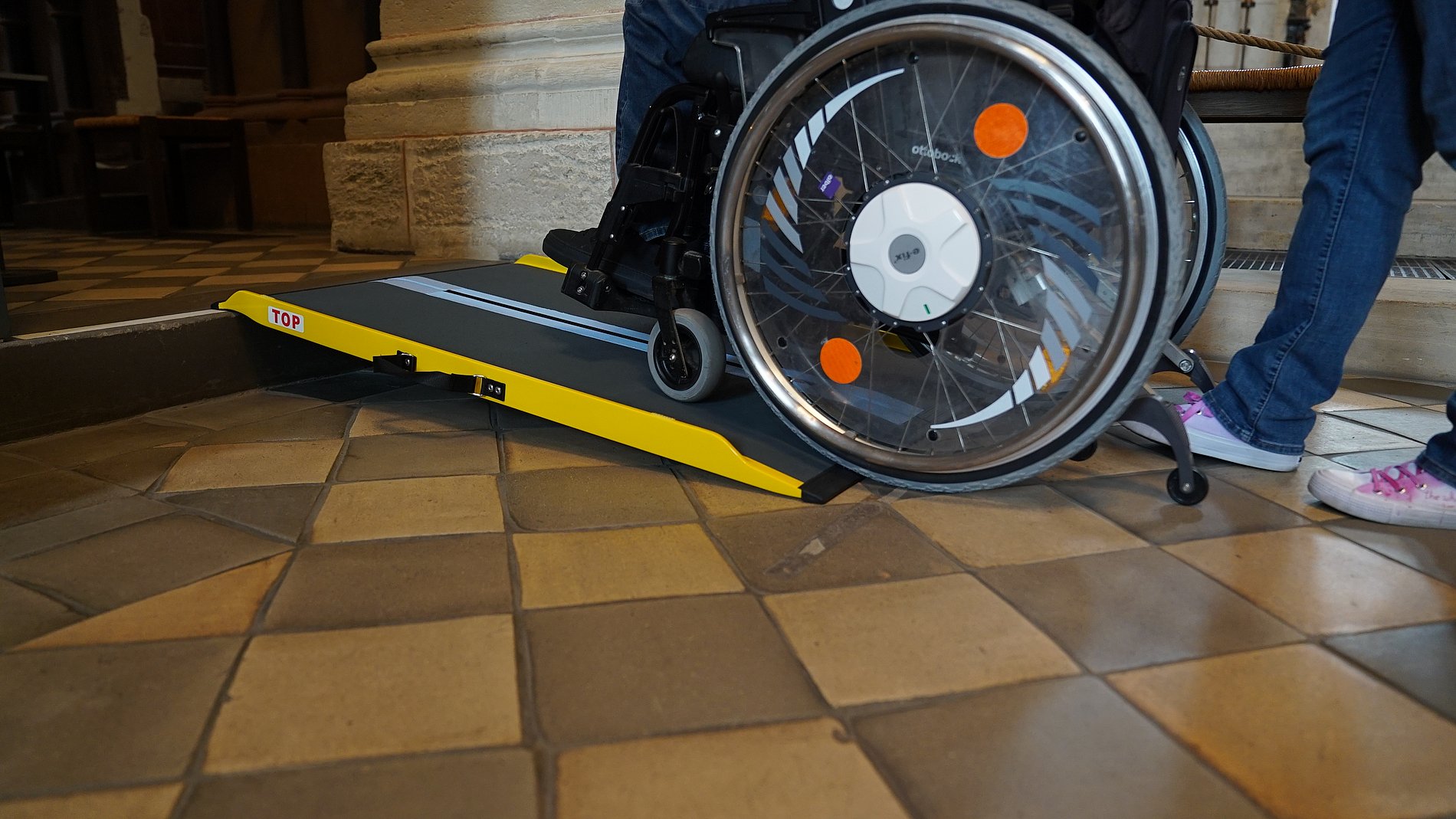 Rampe an einer Stufe mit Rollstuhlrädern am Fußende von der Seite